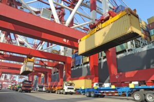 cost of shipping: Image shows TEUs being unloaded from a ship and loaded onto chassis for truck transport