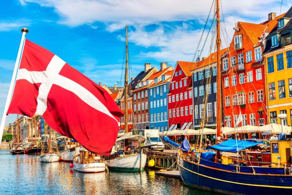 The economic and political development of Denmark Political development: Picture of Danish flag in front of a number of boats in front of a number of brightly colored row houses