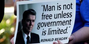 Libertarianism: An image of someone holding up a poster of Ronald Reagan with the quote "Man is not free unless government is limited".
