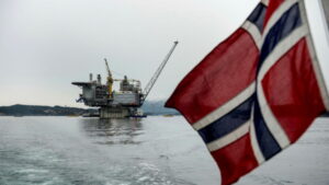 Political development: An image of a Norwegian flag in the foreground with an ocean oil platform in the background