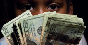 The Federal Reserve creates money: Image of a young man looking at the camera from behind a "fan out" of 20 dollar bills